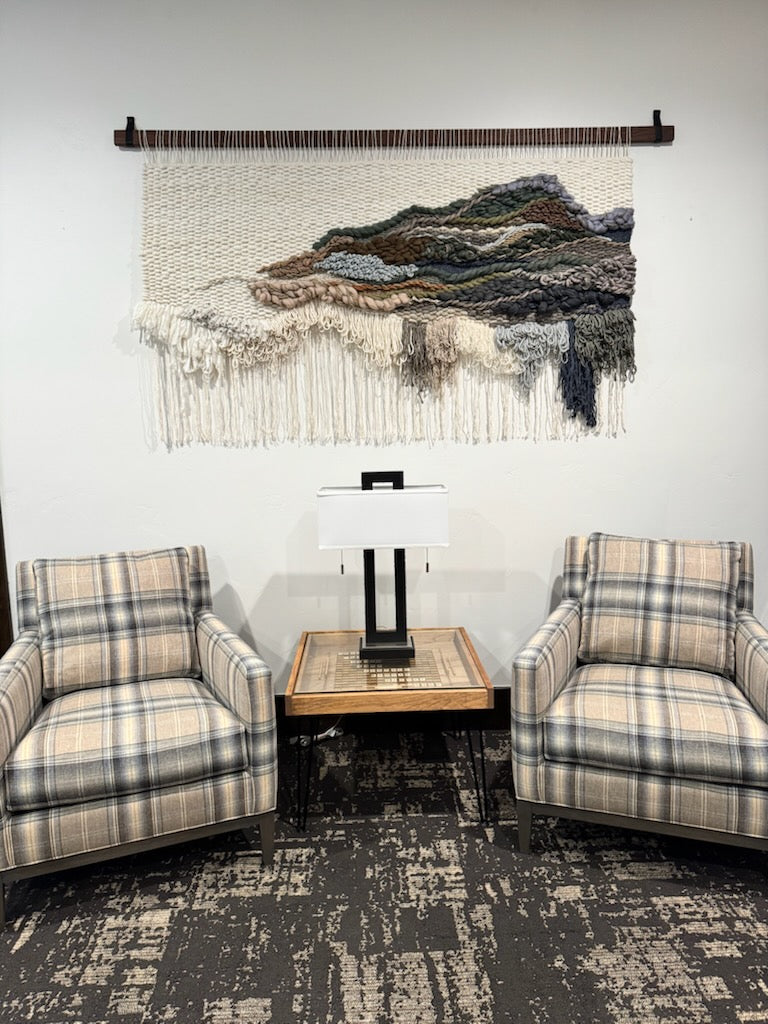 Living room with plaid chairs, a small table, and a woven wall art piece.