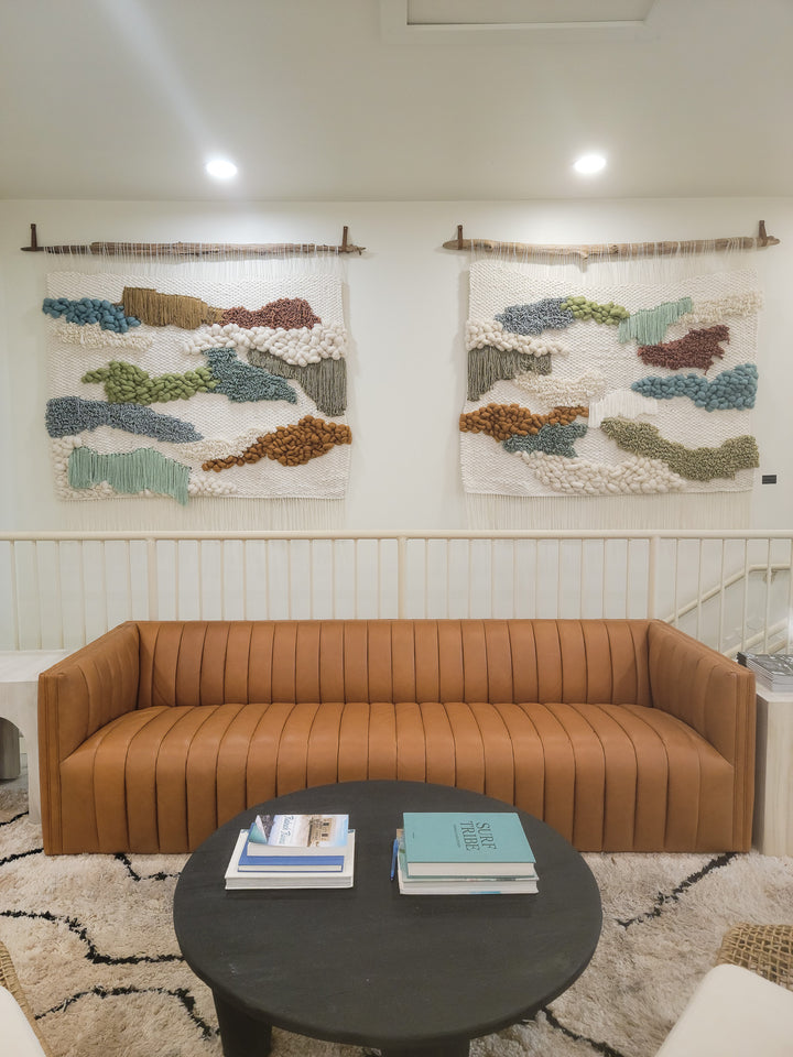 Brown sofa in a room with abstract wall art and a round dark coffee table.