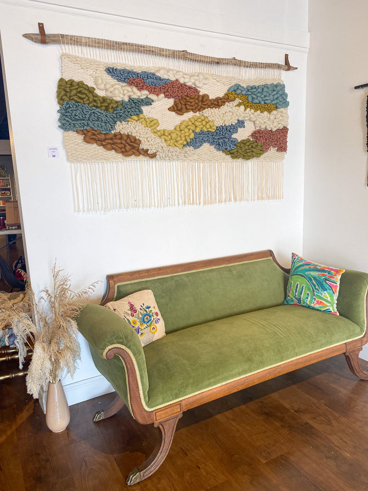 Green sofa with decorative pillows in a room with a textured wall hanging.